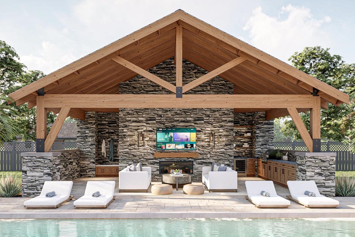An outdoor entertainment area with a pool, stone fireplace, and seating under a wooden-beamed roof, with chaise lounges by the pool.